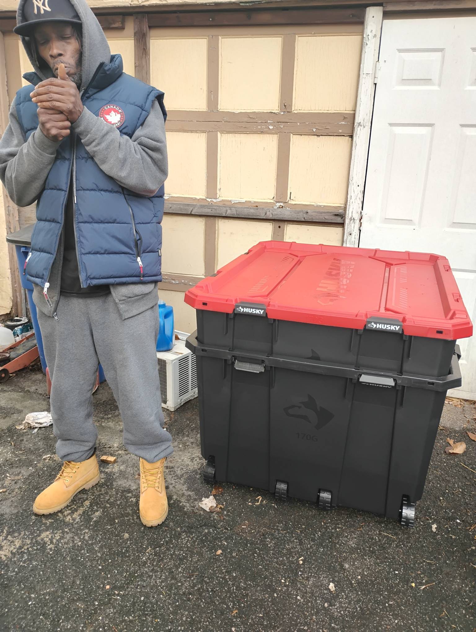 MINDBENDA in an NY cap, gray hoodie and navy vest beside a storage container